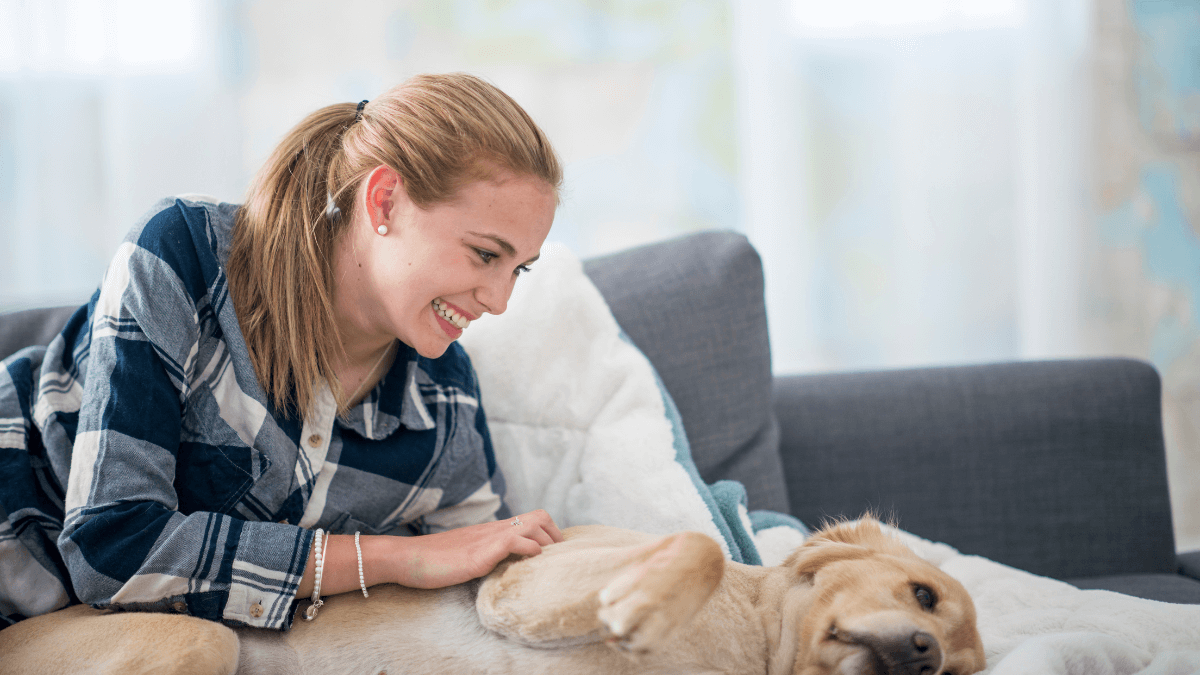 A young woman smiles as she tenderly runs her hand through her furry friend's soft fur, finding comfort and companionship in playing with pets as a remedy for loneliness.
