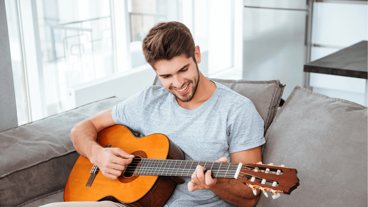 Young man playing guitar in his living room, savoring the benefits of solo living in his 20s.