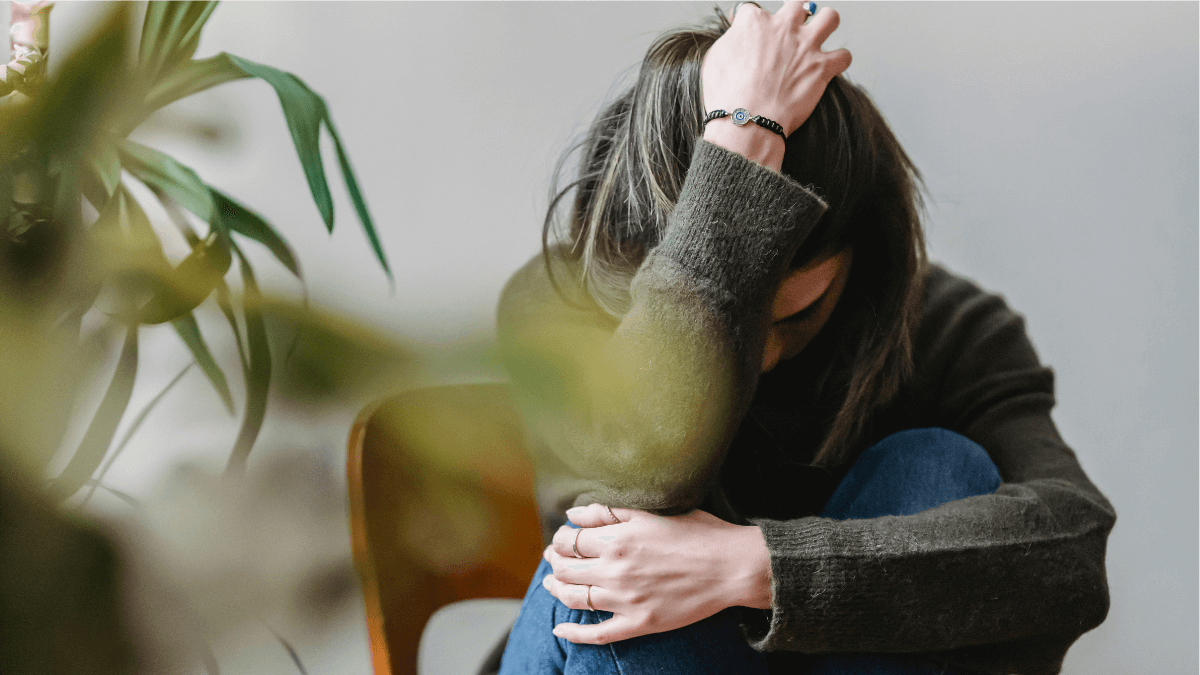 Young woman sitting alone with her face down, reflecting on the challenges of living alone in her 20s.