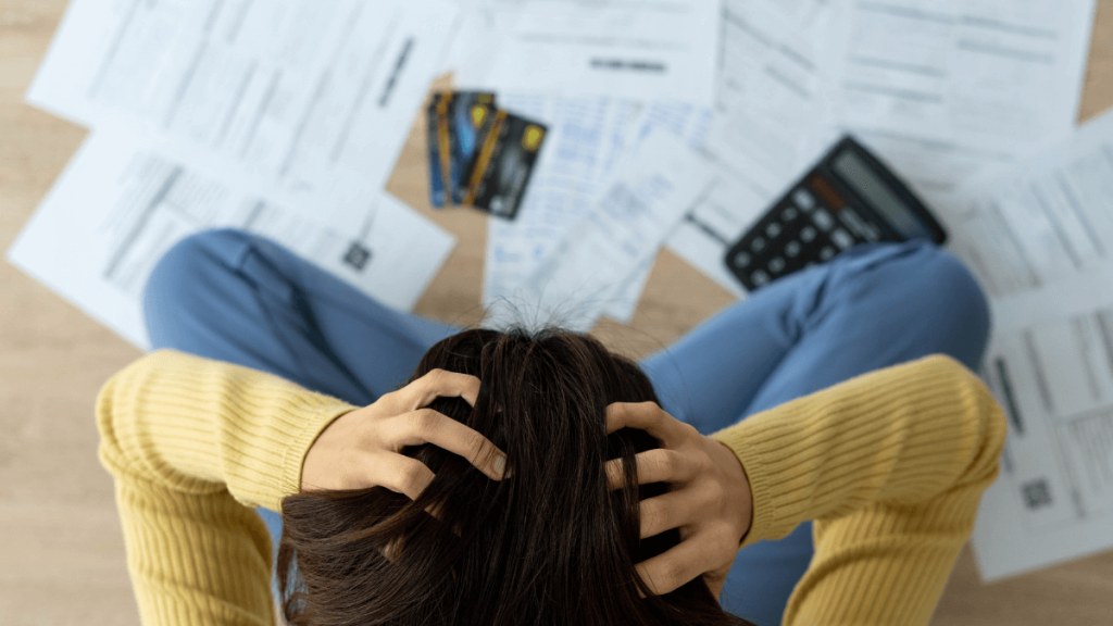 Woman stressed over bills, bank card, calculator, and documents, illustrating the financial disadvantages of living alone.