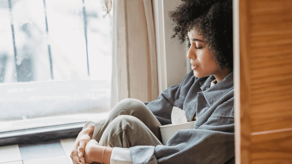 Worried woman sitting alone by a window, emphasizing the social and emotional challenges of living alone.